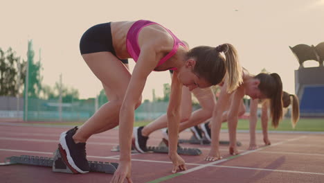 Tres-Mujeres-Jóvenes-En-El-Estadio-En-La-Línea-De-Salida-En-Bloques-Comienzan-La-Carrera-En-Cámara-Lenta